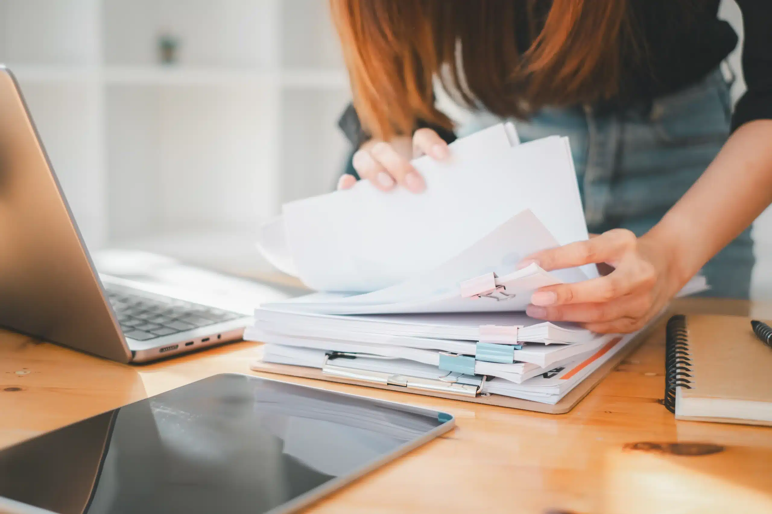 Close-up of a worker organizing paper compliance folders next to a laptop